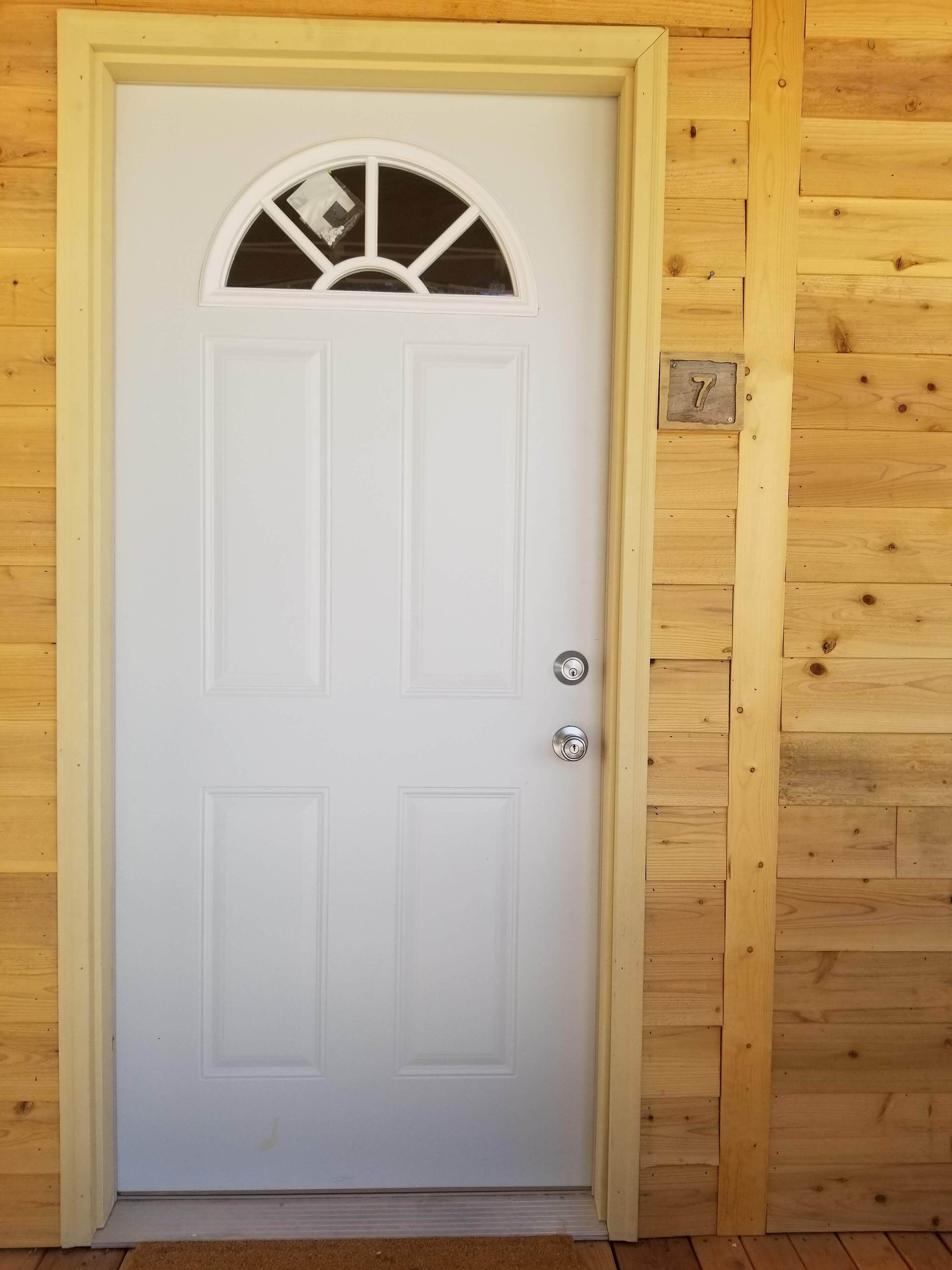 Una puerta blanca con un panel de vidrio en la parte superior, una placa de metal con el número 7, y un picaporte de metal.