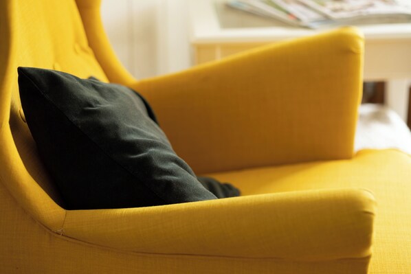 A yellow armchair with a black pillow.
