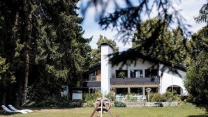 Een modern huis met twee verdiepingen, een groot gazon, een houten schommel en een schoorsteen.