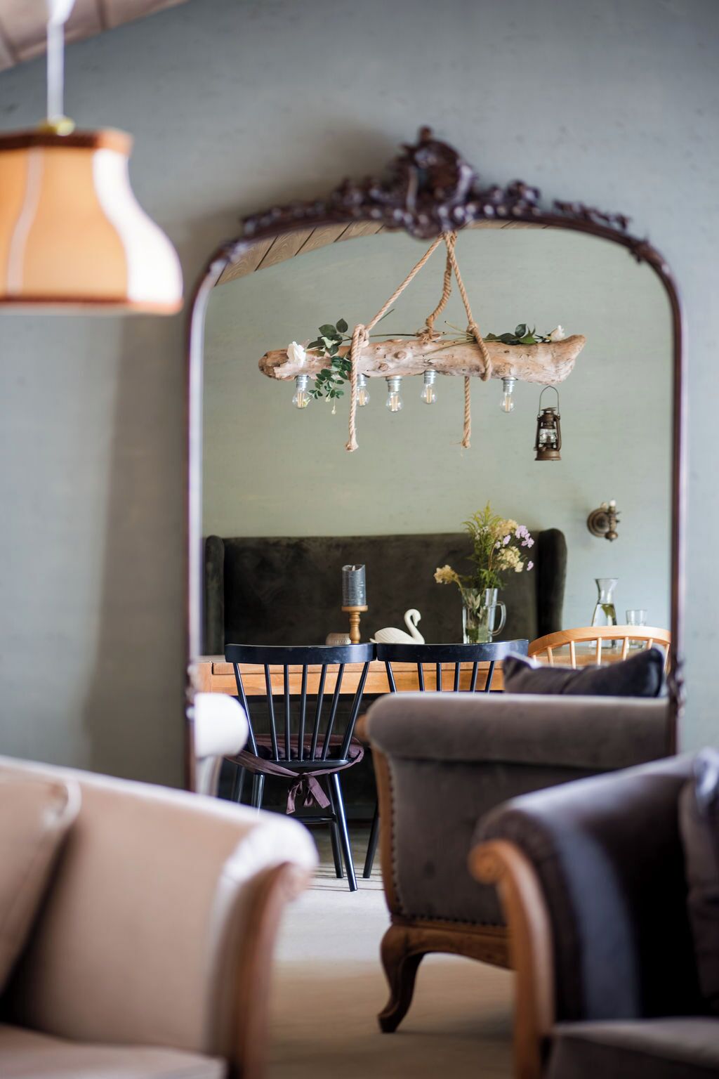 A cozy living room with a rustic chandelier, a large mirror, and a dining area with a modern chair and table.