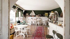 Een gezellig eetgedeelte met witte stoelen en een rood tapijt met patroon, een witte boogvormige doorgang, en een keuken met een groene wand en diverse decoraties.