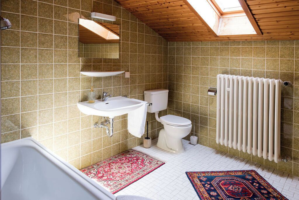 A bathroom with a skylight, a sink, a toilet, a radiator, and a bathtub.