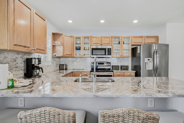 A kitchen with wooden cabinets, a stainless steel refrigerator, a microwave, and a marble countertop.
