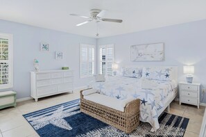 A bedroom with a bed, a nightstand, a dresser, a ceiling fan, and a window with shutters. - Captains Cove 401~heated pool~beach access (Indian Shores)