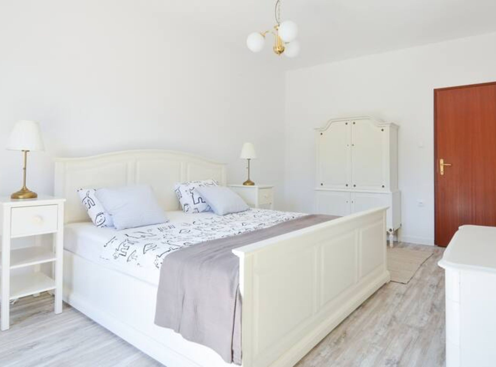 Una camera da letto con un letto bianco, due comodini con lampade, un armadio e una porta in legno.