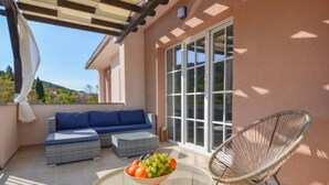 A covered patio with a sofa, a wicker chair, and a table with a fruit bowl. - Apartment Villa Troskot (Pirovac)