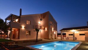 A modern house with a swimming pool, a covered patio, and a well-lit exterior at dusk. - Apartment Villa Troskot (Pirovac)