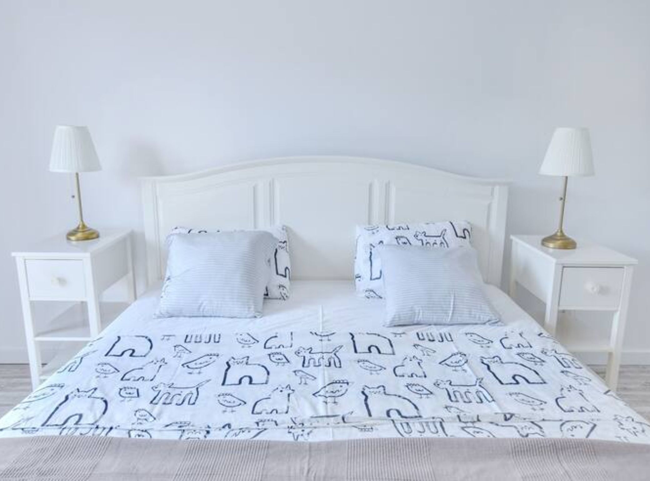 A bed with white bedding and two pillows, flanked by white nightstands with lamps.
