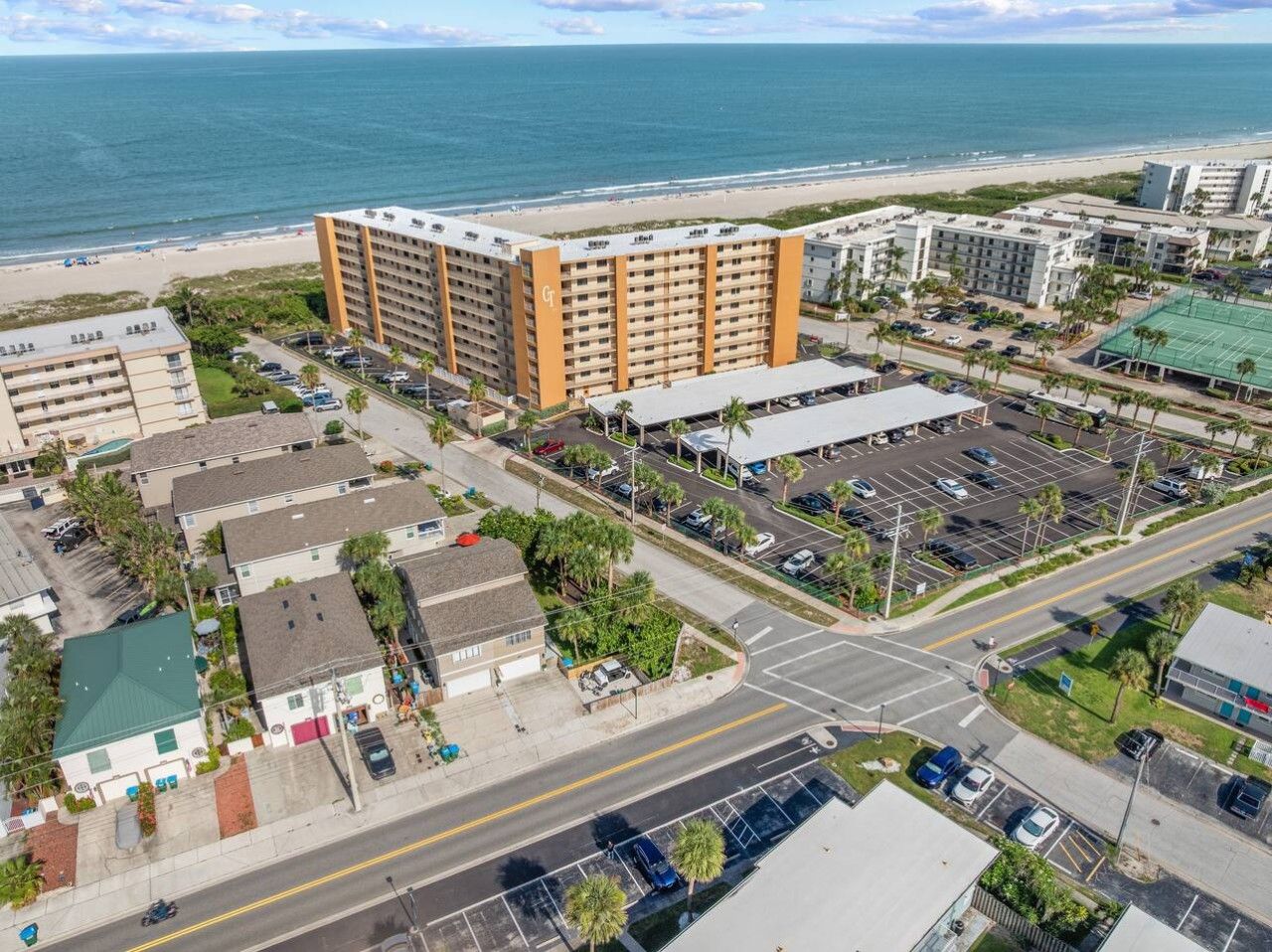 A coastal hotel with multiple floors, a parking lot, and a view of the beach.