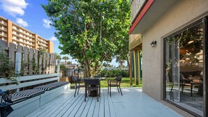 Une terrasse extérieure avec un espace repas, un banc blanc et un grand arbre.