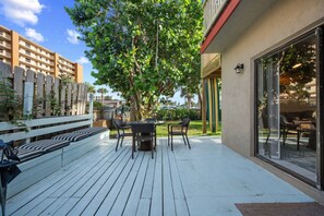Una terraza al aire libre con zona de comedor, un banco blanco y un árbol grande.