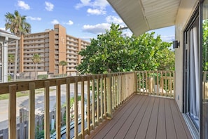 Un balcon en bois offrant une vue sur un immeuble à plusieurs étages et sur une haie verdoyante et touffue.