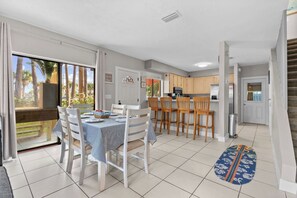 Una cocina moderna con armarios blancos, un comedor con mantel a rayas y vistas a través de la puerta de vidrio.