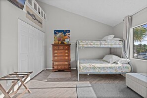 A bedroom with a bunk bed, a wooden dresser, a desk, and a window with a view.