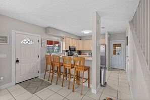Una cocina moderna con una isla central, taburetes de madera y un refrigerador de acero inoxidable.