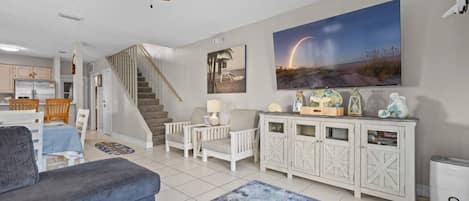 A living room with a sofa, a coffee table, a fireplace, a staircase, and a dining area.
