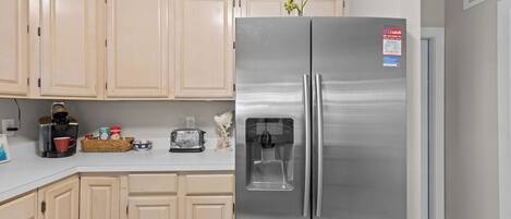 Una cocina con armarios de colores claros, un refrigerador de acero inoxidable, cafetera, tostadora y una pequeña planta.