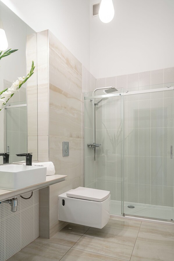 A modern bathroom with a white sink, a large mirror, a toilet, and a glass-enclosed shower area.