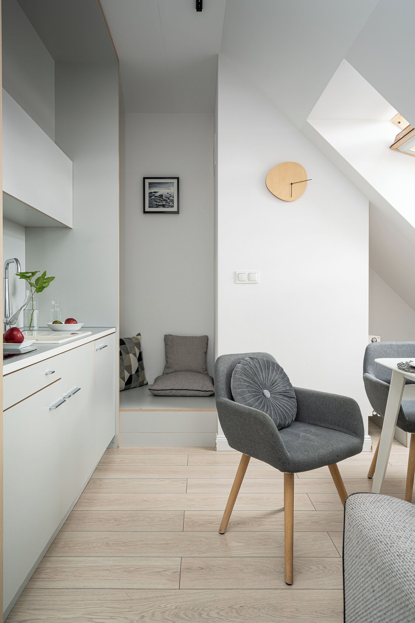 A modern kitchen with white cabinets, a wooden floor, and a dining area with a grey chair and table.
