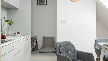 A modern kitchen with white cabinets, a wooden floor, and a dining area with a grey chair and table.