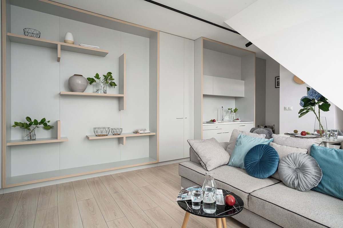 Un salon moderne avec un canapé gris, une table basse et des étagères intégrées ornées d’objets décoratifs.