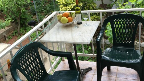 A small outdoor patio with a table and two chairs, surrounded by a white railing.