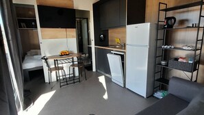 A compact kitchenette with a refrigerator, a small sink, and a dishwasher. There is a dining area with a table and chairs, and a sofa in the corner. - Gabrijela House (Pirovac)