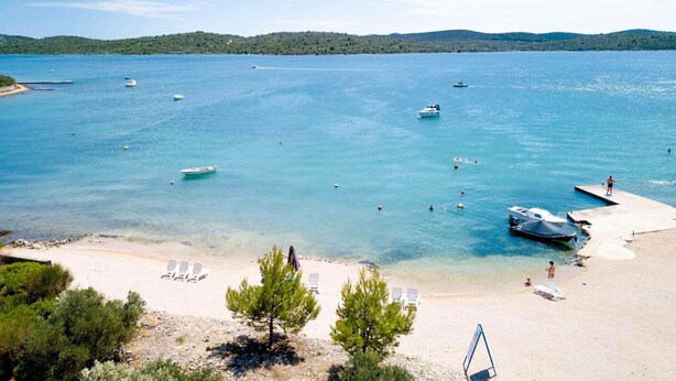 A beach with clear turquoise water, boats, and a sandy shore with lounge chairs. - Gabrijela House (Pirovac)