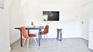 Ein stilvoller Essbereich mit Tisch und zwei Stühlen, einem an der Wand befestigten Fernseher und einem Mülleimer.