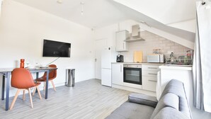 Eine moderne Küche mit weißen Schränken, einer Mikrowelle und einem Herd. Es gibt eine Essecke mit Tisch und Stühlen, und ein graues Sofa im Vordergrund.