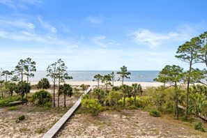 A beach with a wooden boardwalk, trees, and a clear view of the ocean.