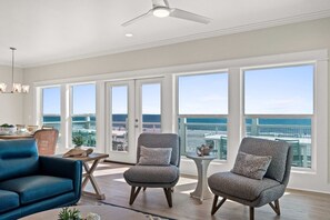 A spacious room with large windows, a ceiling fan, and two armchairs with cushions. - Dolphins Leap: New Build, Beachfront, Private Pool (St Joe Beach)