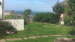Un giardino sul retro con erba, vista sul mare, un muro bianco e una recinzione in legno.