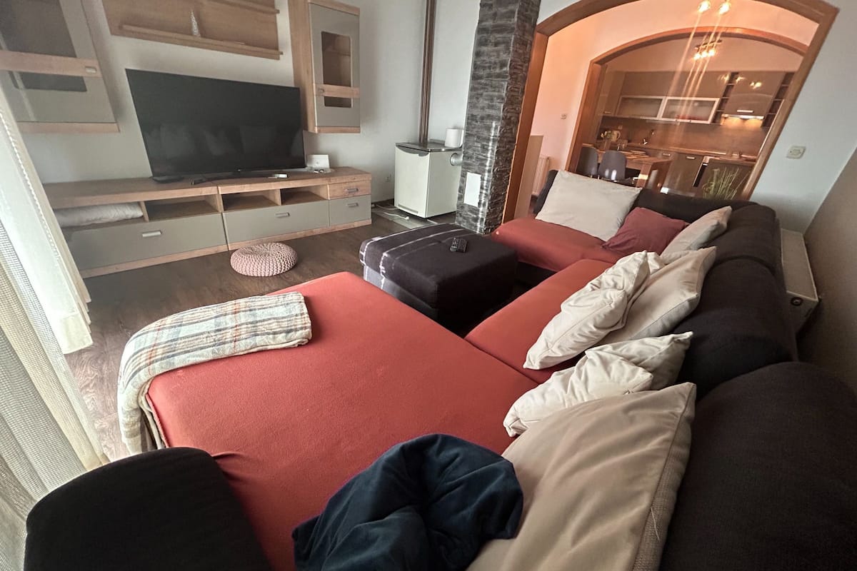 A modern living room with a sofa, ottoman, and a TV on a wooden stand.