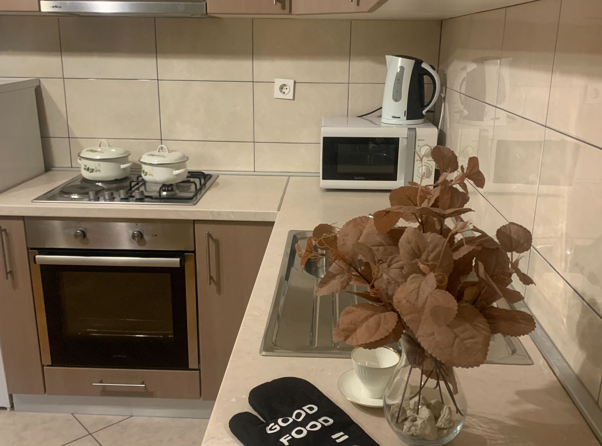 A kitchen with a stove, oven, microwave, and a kettle on the countertop.