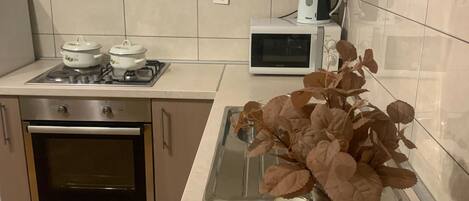 A kitchen with a stove, oven, microwave, and a kettle on the countertop.