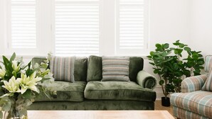 A green velvet sofa with striped pillows, a small table, and a potted plant.