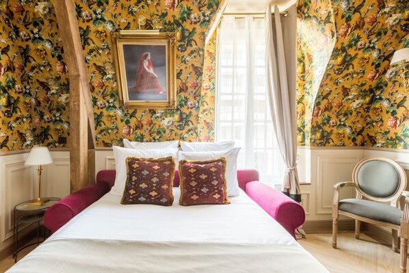 A room with a bed, two pillows, a chair, a lamp, and a painting on the wall.