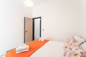 Una habitación de hotel con una cama, una colcha naranja, almohadas blancas y una toalla doblada sobre la cama.