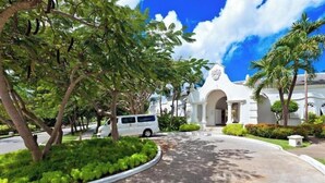 Um edifício branco com uma entrada central em arco, rodeado por vegetação exuberante e palmeiras.
