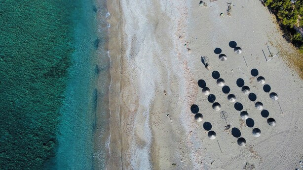 Vista aerea di una spiaggia con acque cristalline turchesi e una battigia sabbiosa.