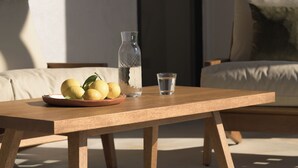 Un tavolo di legno con una bottiglia d'acqua e un bicchiere, un piatto con limoni e un divano sullo sfondo.