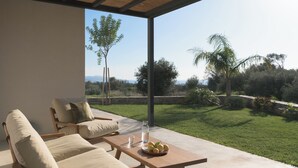 Una terrazza esterna con tavolo in legno, due sedie imbottite e vista su un paesaggio erboso con alberi.