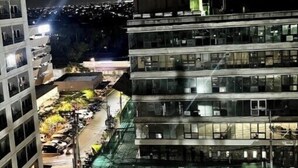Un immeuble à plusieurs étages doté d’une terrasse sur le toit, de palmiers et d’un espace de stationnement.
