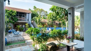 A poolside area with lounge chairs, a small table, and a view of a building with a tiled roof. - Lan Anh Garden Resort (Phu Quoc)