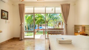A hotel room with a bed, a bench, a view of a pool and palm trees, and a sliding glass door. - Lan Anh Garden Resort (Phu Quoc)