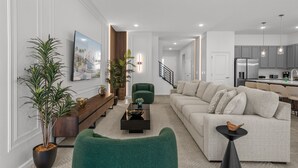 A modern living room with a sofa, coffee table, and green armchair. There is a kitchen area with cabinets and a refrigerator in the background.