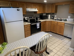 A kitchen with wooden cabinets, a white refrigerator, a stove, a microwave, and a dining table with chairs.