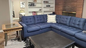 Un soggiorno con un divano ad angolo blu, un tavolino da caffè con piano in vetro e una libreria bianca con oggetti decorativi.