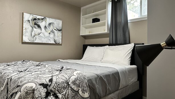 Una camera da letto con un letto, una mensola a parete, un quadro e una finestra con tende.